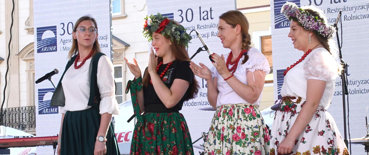 Cztery kobiety ubrane w stroje ludowe na scenie, w tle informacje 30 lat ARiMR