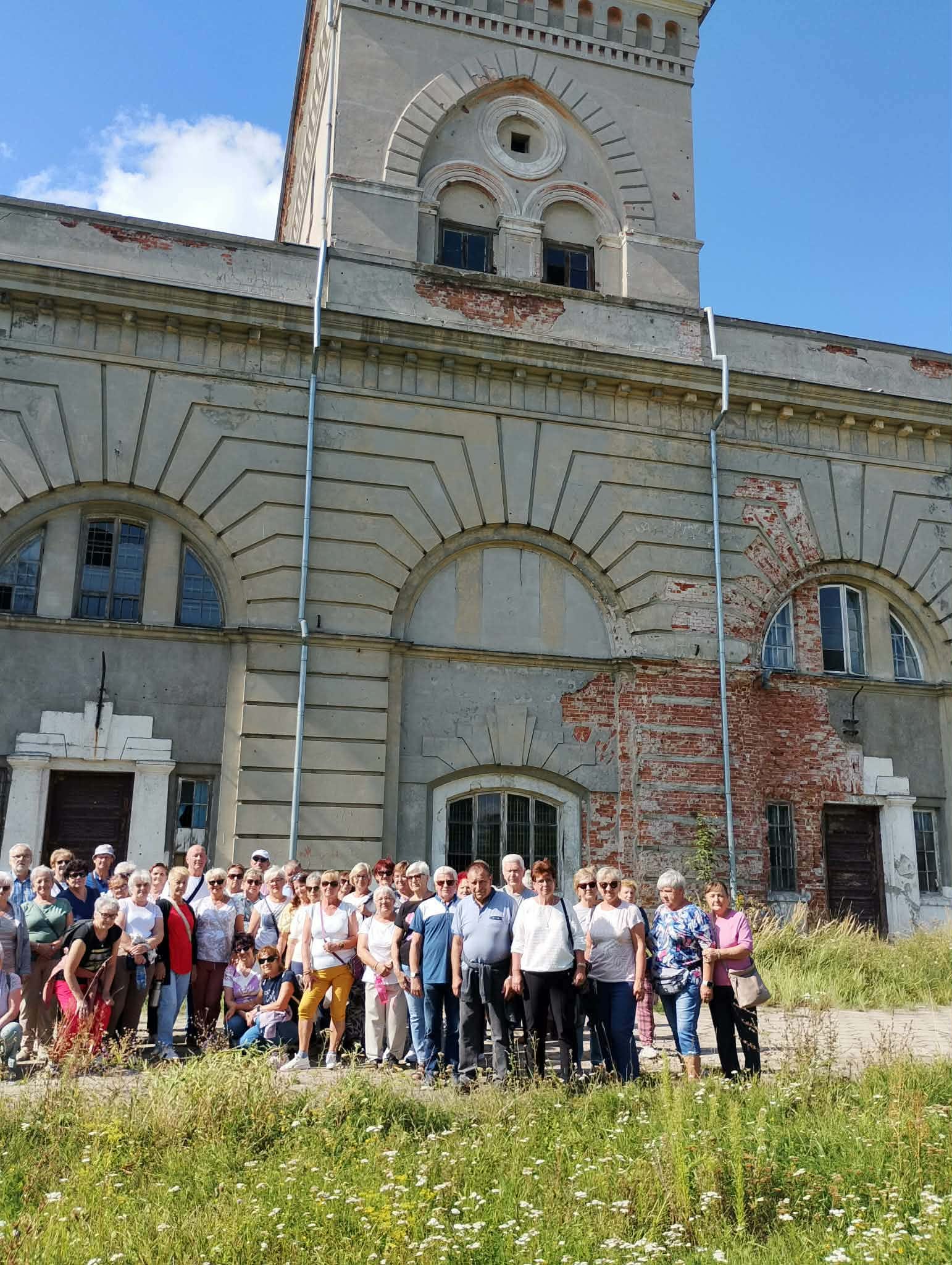 Zdjęcie grupowe, wykonane w pozycji wertykalnej, przedstawiające seniorów na tle starego budynku