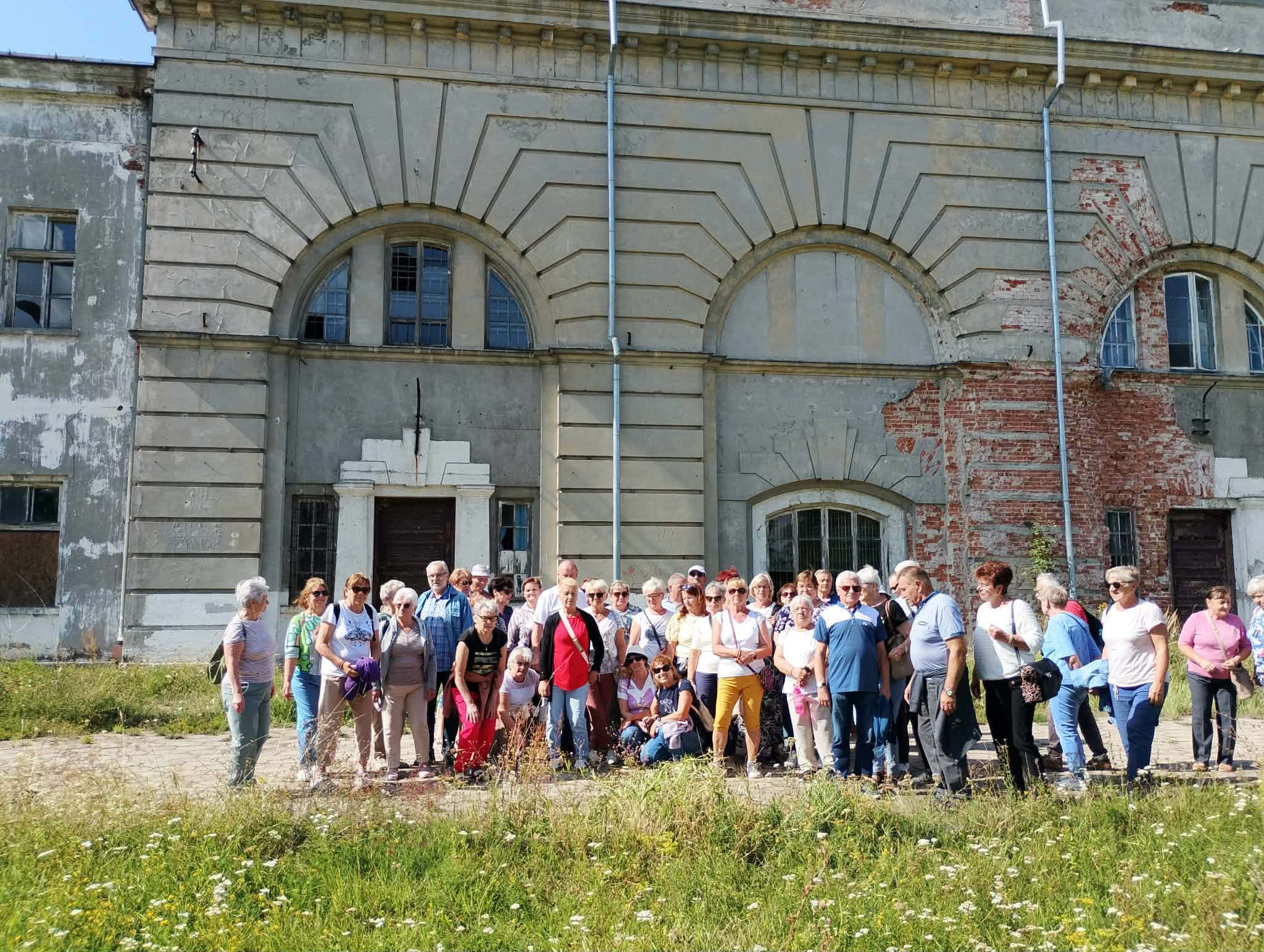 Zdjęcie grupowe, wykonane w pozycji horyzontalnej, przedstawiające seniorów na tle starego budynku